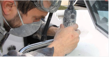 Yacht repair professional uses a dremel to precisely cut away and replace damaged fiberglass on a boat. 
